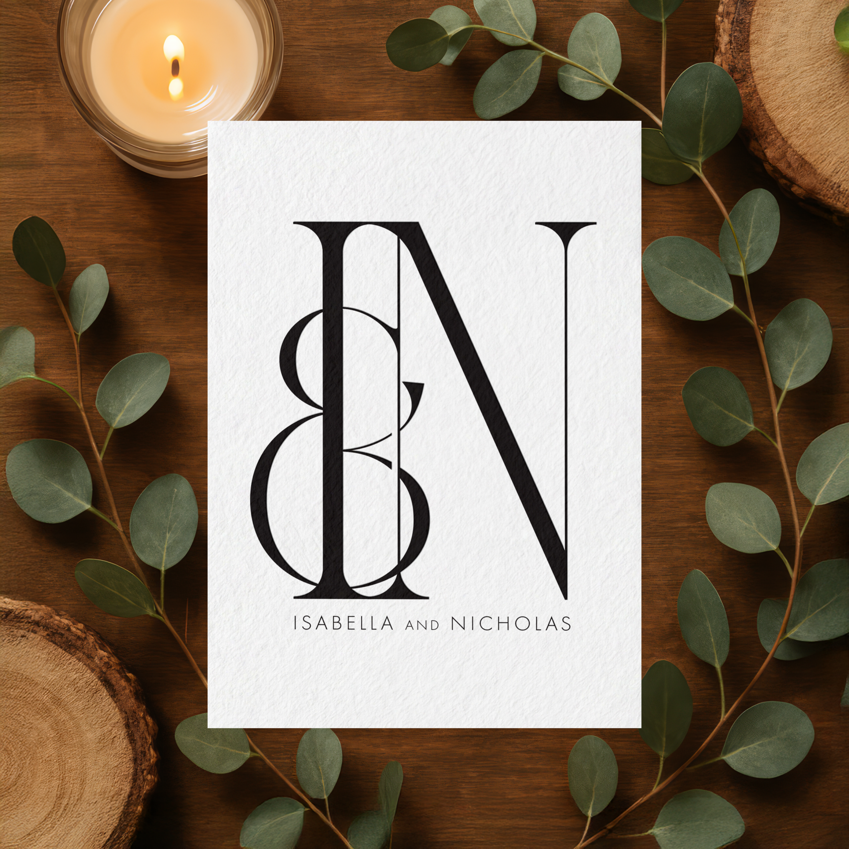 Black and White wedding monogram for Isabella and Nicholas on textured white paper with eucalyptus greenery, a candle, and wood slices, a lit candle, and wood slices, matching the mockup style used across